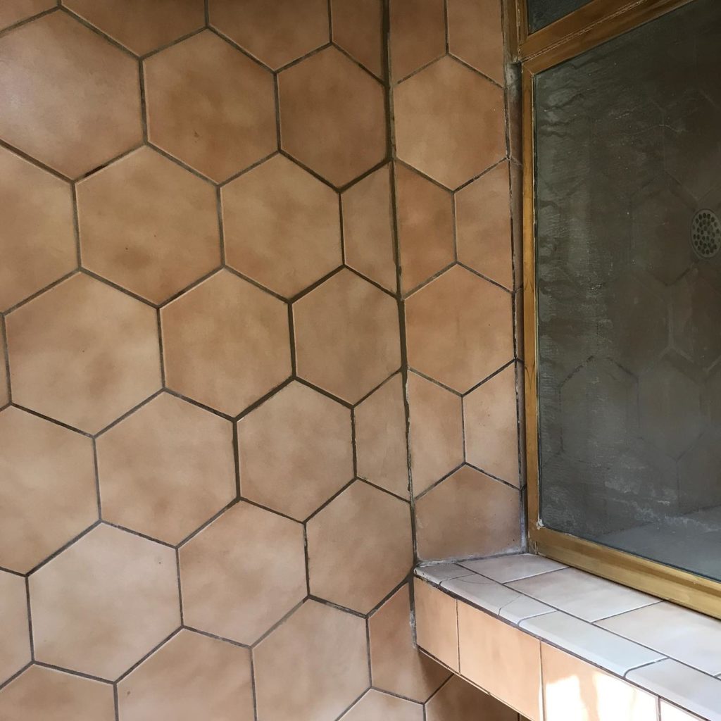 Shower area with large hexagonal tan tiles and a glass door with a brass frame.