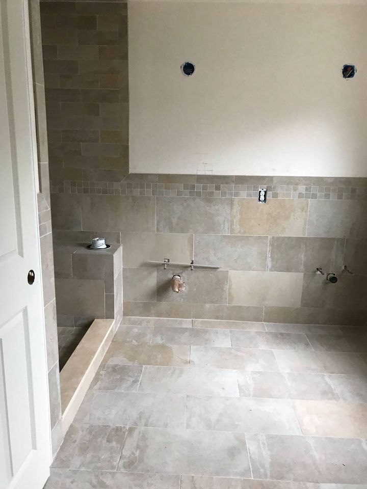 Bathroom under renovation with tiled floors and walls, plumbing fixtures exposed, and space prepared for a vanity or sink installation.