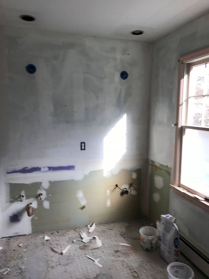 Bathroom in early renovation stage with unfinished walls, exposed plumbing, and construction materials on the floor.